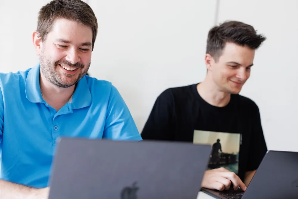 Zwei Teammitglieder lächeln bei der Arbeit an ihren Laptops
